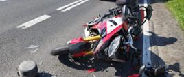Motocykl leży na drodze po zderzeniu z samochodem dostawczym. W tle stoi karetka pogotowia