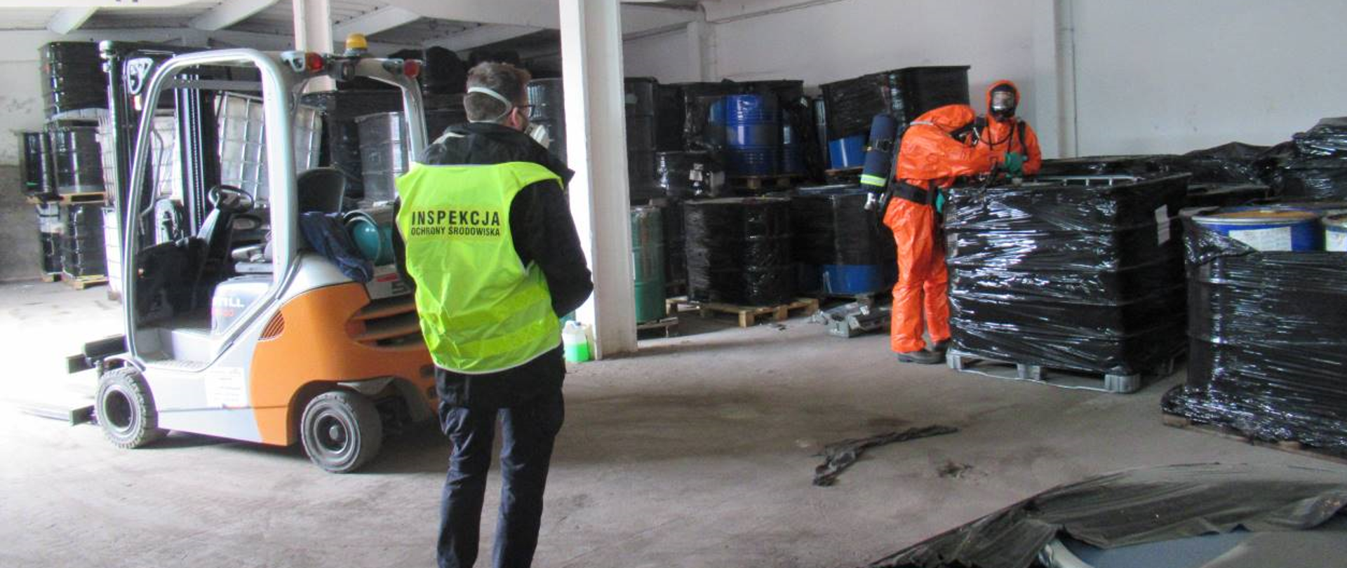 Osoby w kombinezonach ochronnych kontrolują zbiornik na palecie