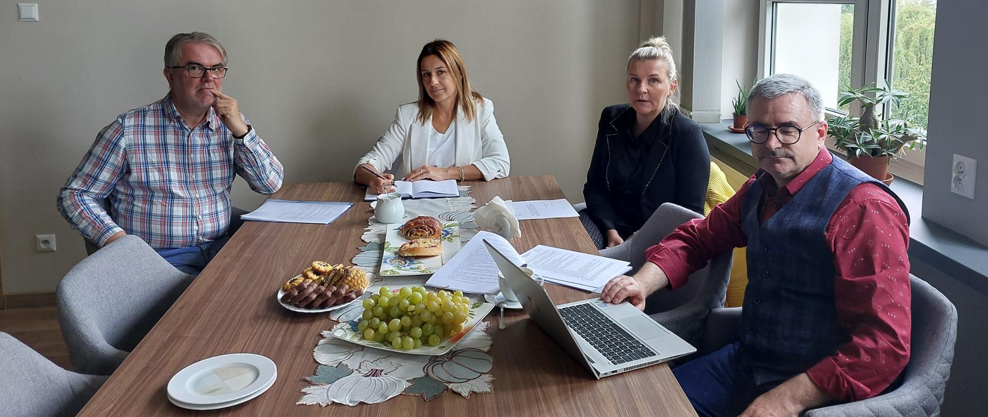 Dwie kobiety i dwóch mężczyzn siedzący przy stole konferencyjnych, jeden z mężczyzn ma przed sobą laptop