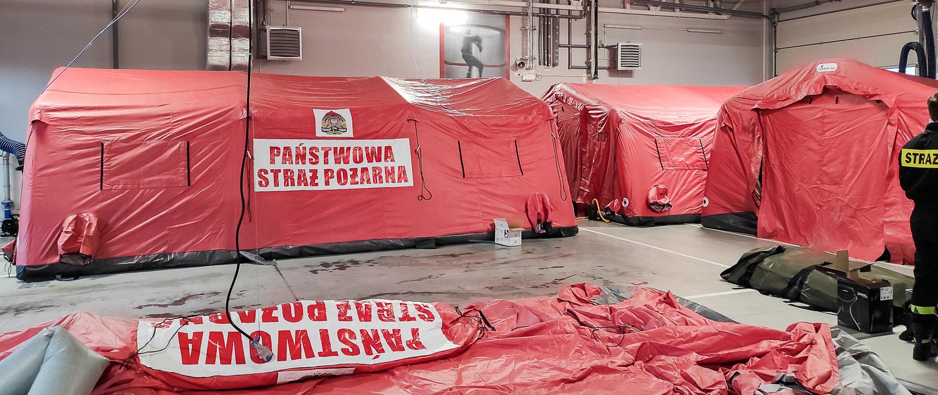 Zdjęcie przedstawia cztery namioty pneumatyczne koloru pomarańczowego. Trzy namioty napompowane gotowe do użycia. Jeden namiot w trakcie przygotowania do napompowania powietrza.