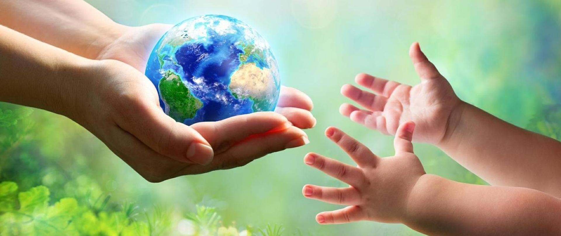 Na zdjęciu widać kulę ziemską trzymaną w kobiecych rękach i wyciągnięte w jej kierunku małe rączki dziecka.