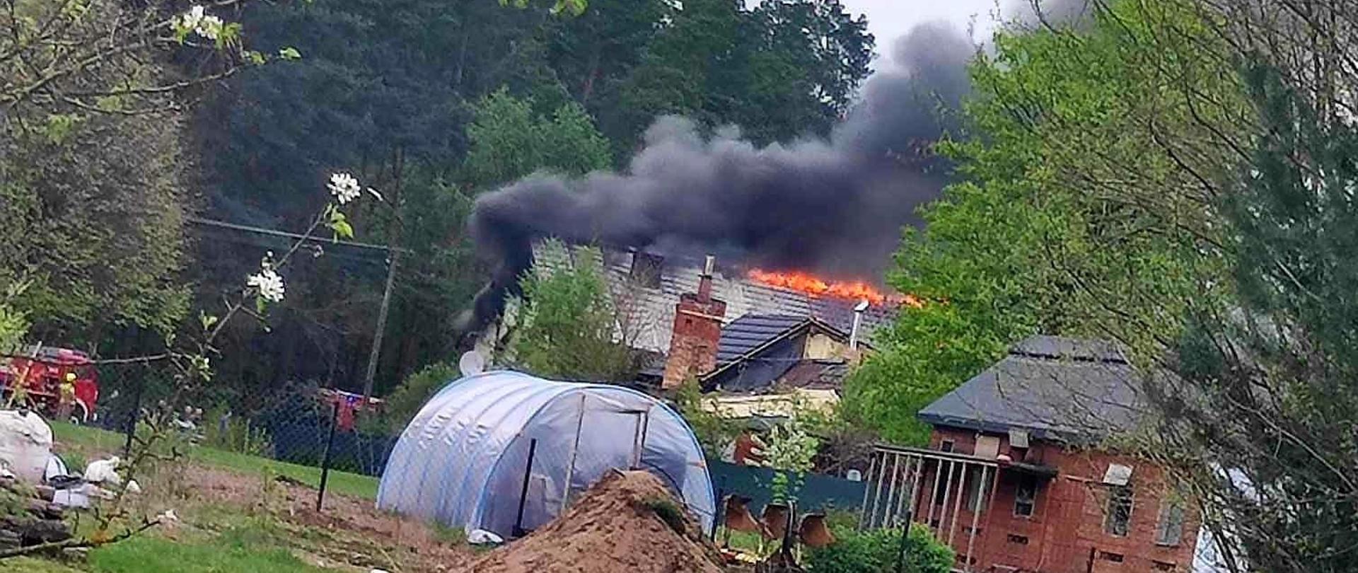 Pali się dach domu. Widoczny ogień i czarny dym.