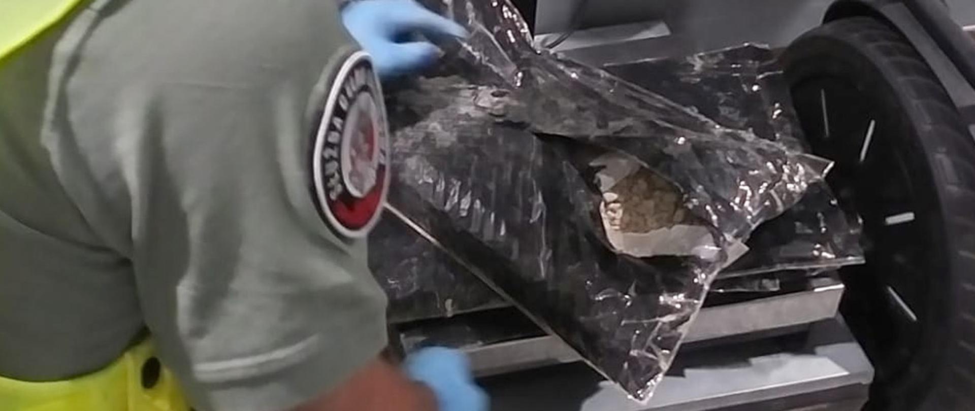 Funkcjonariusz Służby Celno-Skarbowej trzyma worek z granulatem.