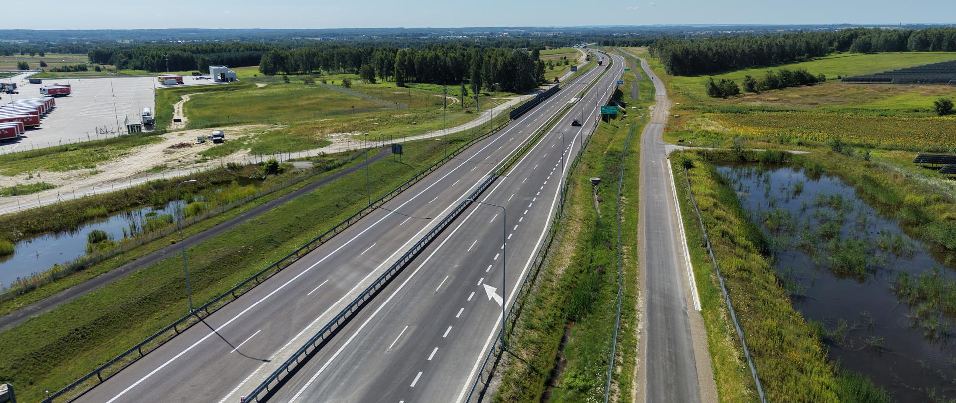 Na zdjęciu widać drogę ekspresową S19 z lotu ptaka. W oddali widać wiadukt. Widać, dwie jezdnie, samochody jadące po drodze, bariery rozdzielające obie jezdnie. Jest słonecznie. 