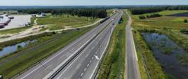Na zdjęciu widać drogę ekspresową S19 z lotu ptaka. W oddali widać wiadukt. Widać, dwie jezdnie, samochody jadące po drodze, bariery rozdzielające obie jezdnie. Jest słonecznie. 