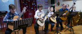 Na scenie prezentuje się zespół gitarowy. Gra nauczyciel i uczniowie gitary