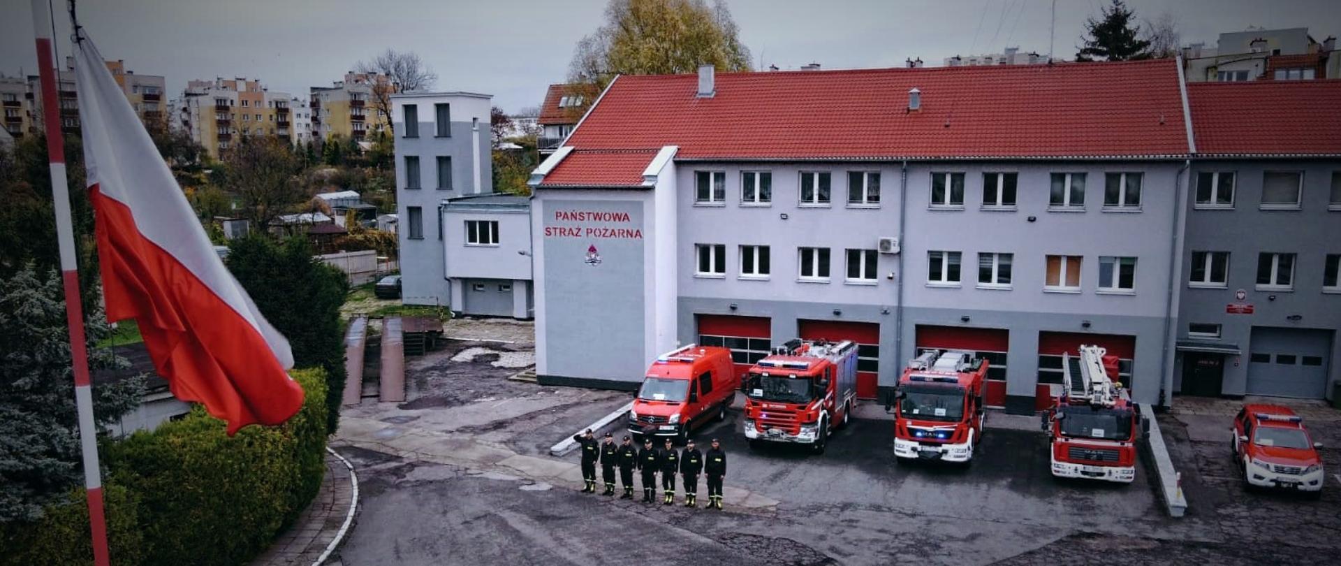Flaga Rzeczypospolitej Polskiej na tle remizy strażackiej.