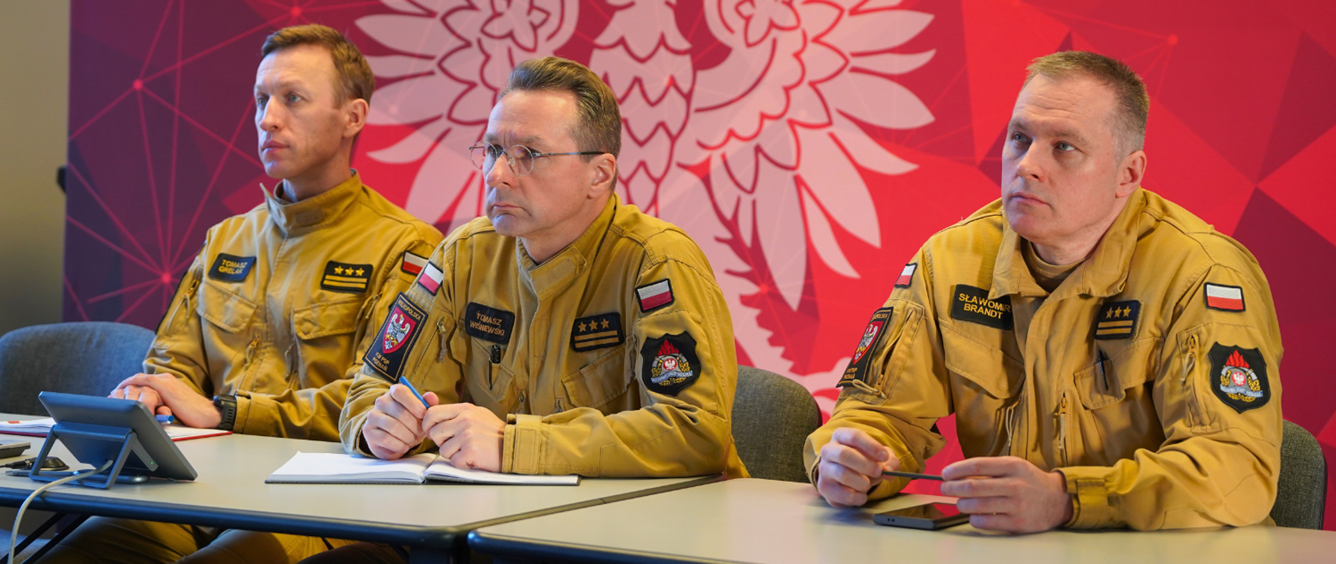 Na zdjęciu zastępcy wielkopolskiego komendanta wojewódzkiego PSP uczestniczą w sali prezydialnej w wideokonferencji, siedząc za stołem.