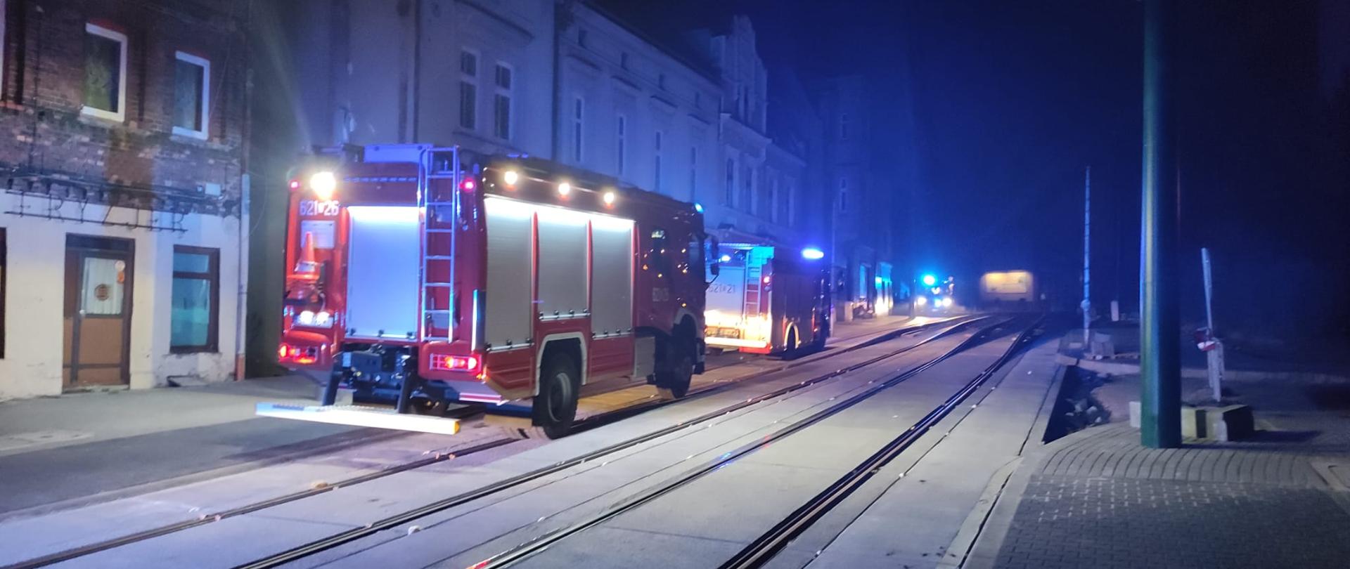 Zdjęcie przedstawia dwa wozy strażackie z włączonymi sygnałami świetlnymi stojące przed budynkiem przy ulicy Łagiewnickiej.