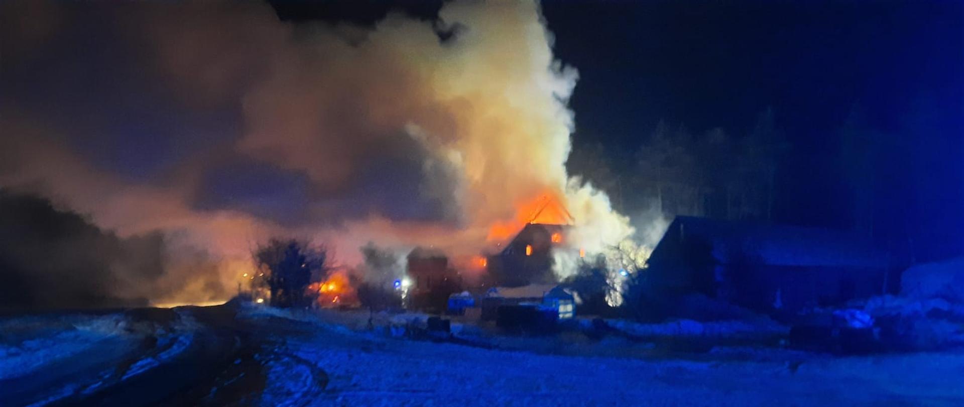 widok płonącego domu z oddali, na zdjęciu widoczne płomienie wychodzące z dachu