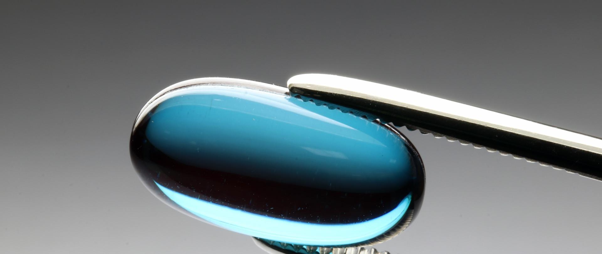 Szczypce trzymające niebieską tabletkę.