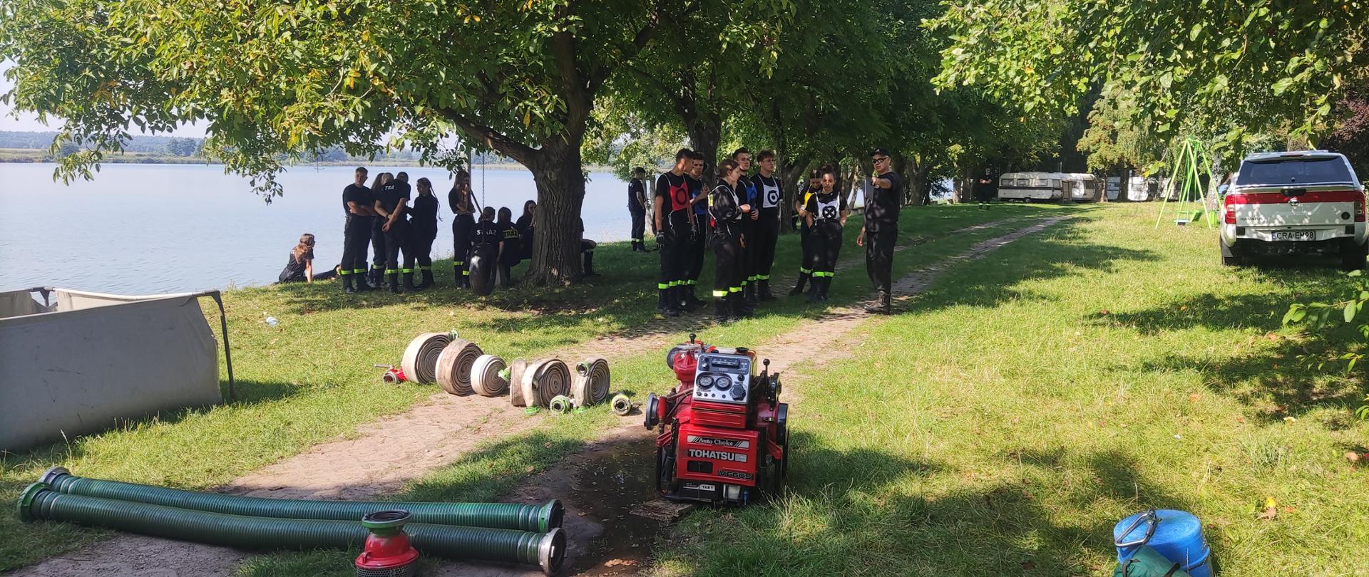 Zdjęcie przedstawia uczniów klas mundurowych na obozie nad jeziorem gopło, sprzęt strażacki, samochód operacyjny