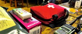 Uczestnicy szkolenia siedzą przy stole i słuchają prowadzącego; na pierwszym planie apteczka pierwszej pomocy i sprzęt ratunkowy.