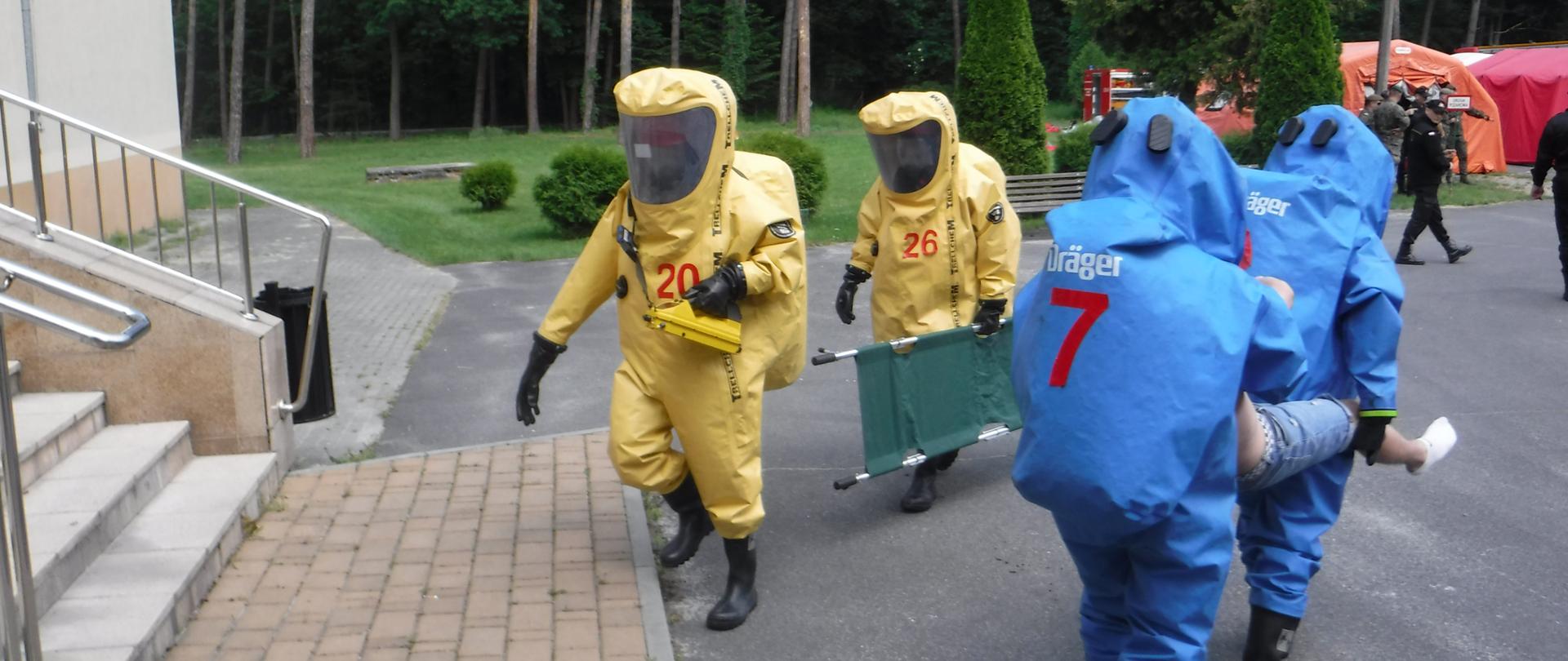 Na zdjęciu widzimy dwie roty, które ubrane są w kombinezony gazoszczelne i ewakuujące poszkodowanych z budynku. 