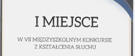 Na dyplomie, w centralnej części, na białym tle widnieje czarny napis I miejsce na VII Międzyszkolnym Konkursie z Kształcenia Słuchu dla Macieja Marcińca Państwowa Szkoła Muzyczna I stopnia im. Witolda Lutosławskiego w Jaśle. W dolnej części widnieje czerwona pieczęć Zespołu Szkół Muzycznych w Gorlicach z podpisem dyrektora oraz podpisy jury konkursu. Na samym dole dyplomu, w prawym rogu widnieje miejsce i data konkursu – Gorlice, dnia 24.05.2023 r. Kolorystyka zdjęcia jest biało-żółto- niebiesko-granatowo-czerwono- czarna. Elementy graficzne tła o kolorystyce niebiesko-granatowej z delikatnymi liniami w kolorze żółtym znajdują się w prawym górnym rogu oraz w lewym dolnym rogu.