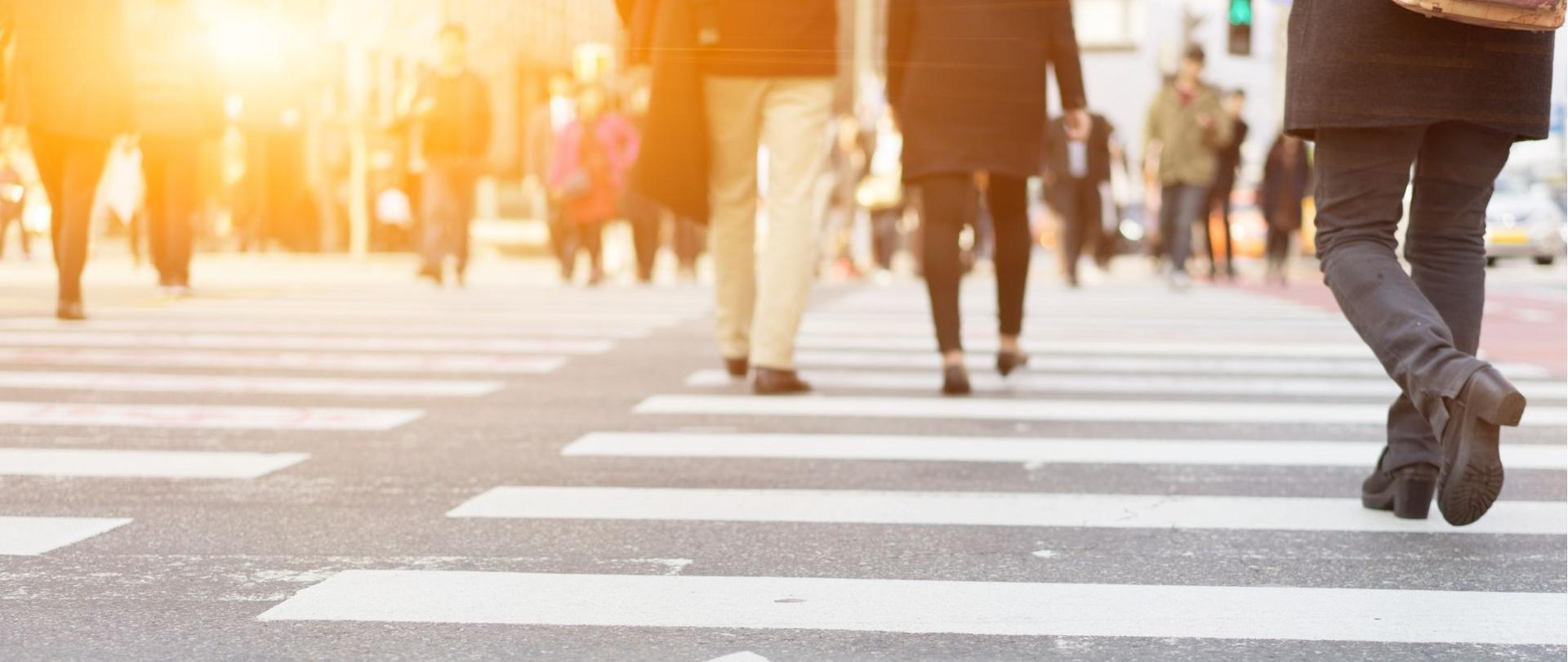 Zdjęcie przedstawia oznakowane przejście dla pieszych, po którym poruszają się ludzie