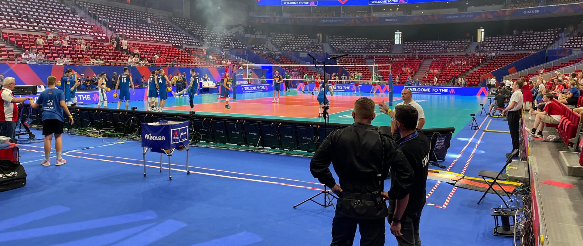 Hala ERGO ARENA. Po środku boisko do siatkówki na którym grają zawodnicy. Tyłem stoi strażak PSP i OSP którzy zabezpieczają imprezę i sprawdzają stan zabezpieczeń na hali