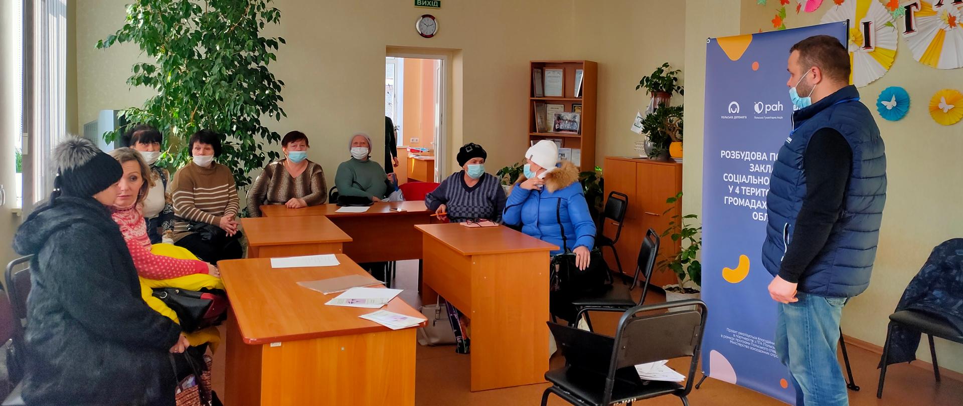 Kilka osób w kurtkach siedzi przy biurkach.