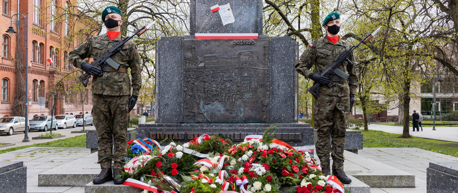 Pomnik Wolności. Przed pomnikiem leżą wiązanki kwiatów. Po prawej i lewej stronie stoją żołnierze na warcie.