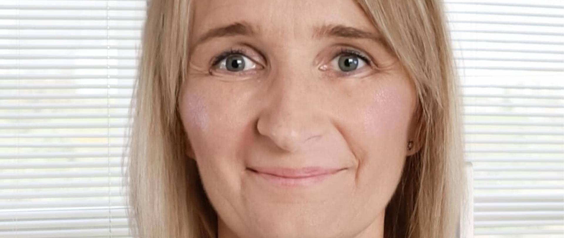 Młoda kobieta z krótkimi blond włosami w niebieskiej koszuli z uśmiechem na twarzy 