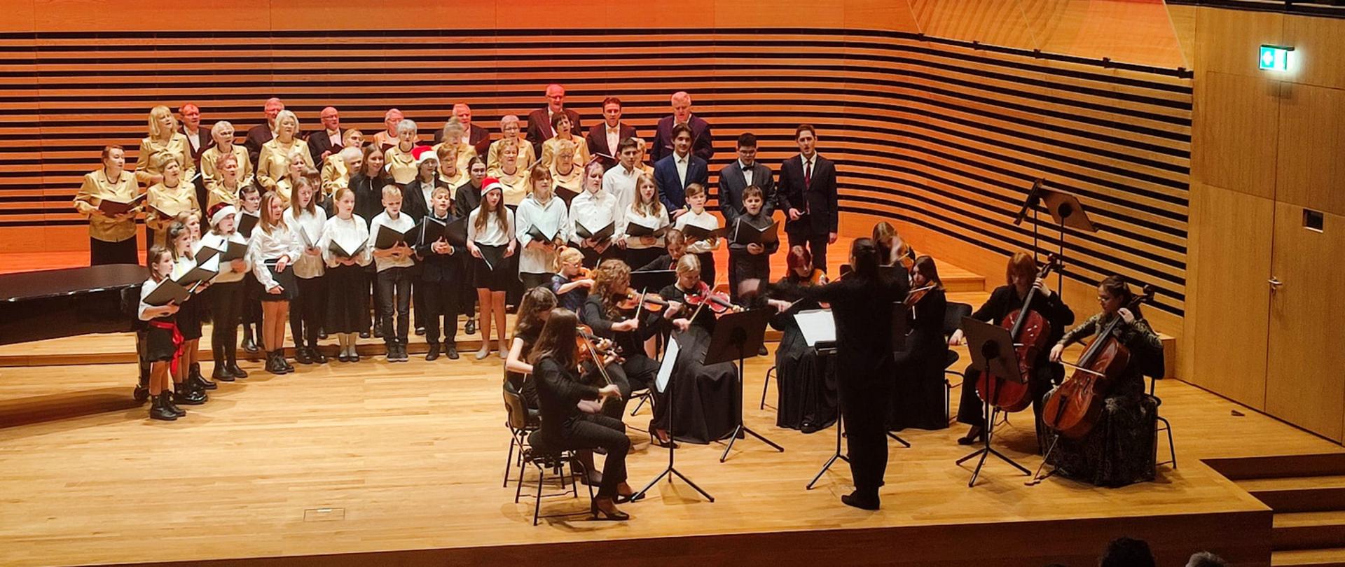 Grająca orkiestra smyczkowa, Pani Dyrygent, śpiewający chór PSM oraz Chór Miejski na scenie sali koncertowej PSM