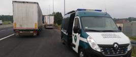 Kontrole drogowe ciężarówek zatrzymanych przez patrol ITD. Na pierwszym planie przód oznakowanego radiowozu ITD typu furgon. W tle stoją obok autostrady A4 dwa zestawy ciężarowe.