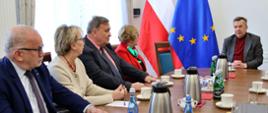 Przy owalnym stole siedzi kilka osób, u szczytu stołu minister Wieczorek, za nim pod ścianą flagi Polski i UE.