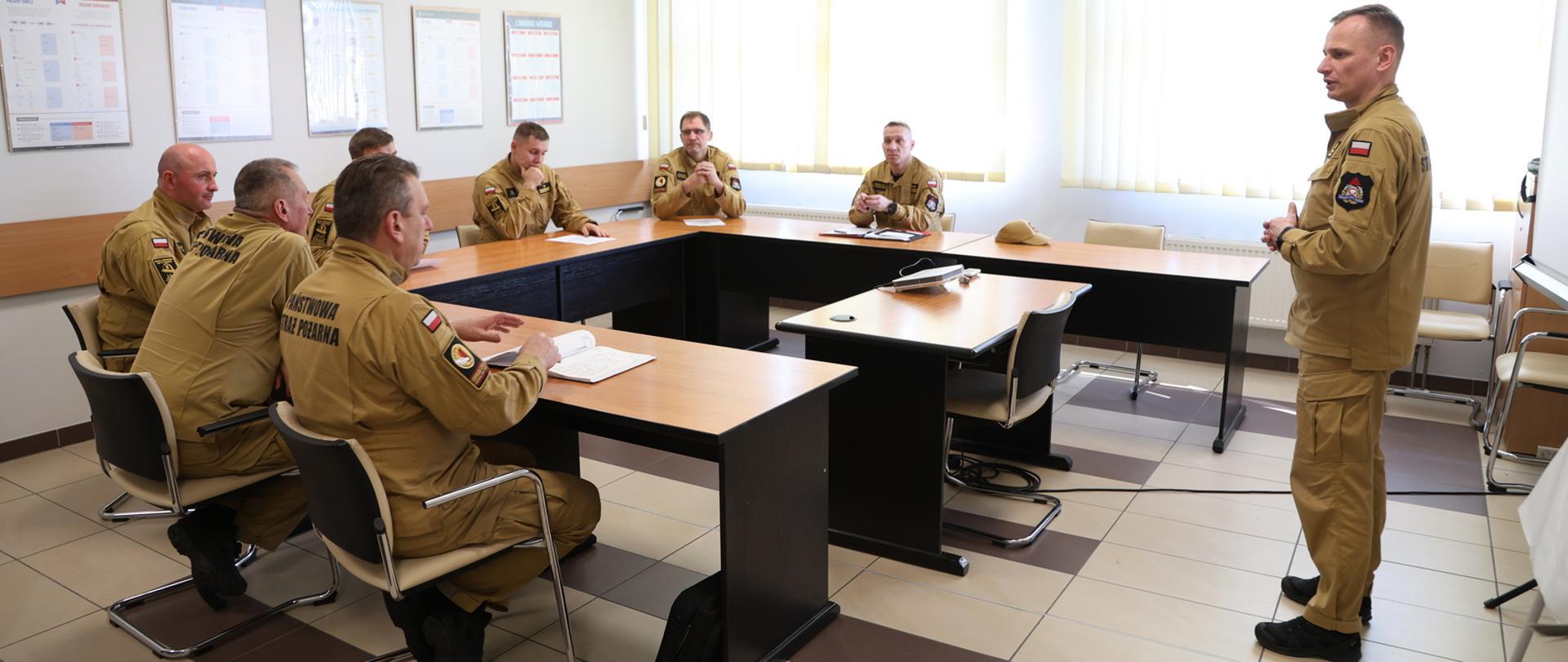 Sala wykładowa, p.o. Komendant Centralnej Szkoły PSP przemawia do siedzących za ławkami ustawionymi w podkowę przedstawicieli wydziałów nauczania szkół aspirantów