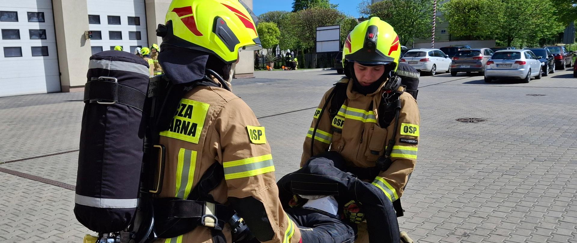 Dwóch strażaków w ubraniu specjalnym niesie manekina po placu JRG Tczew.