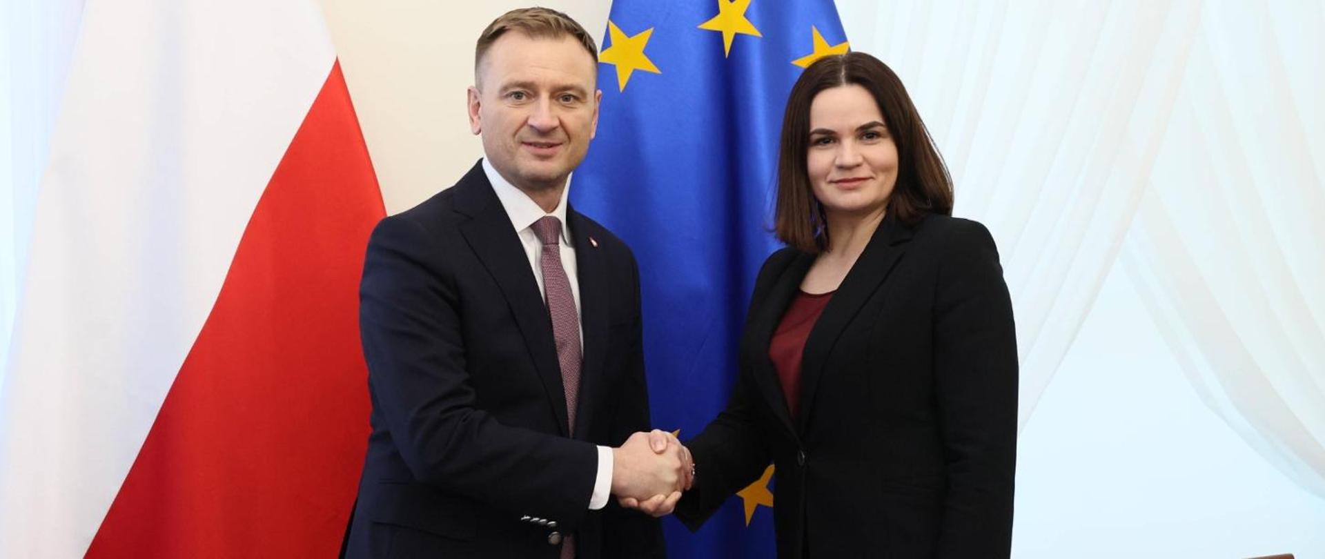 man and woman in suits shake hands with UE and Polish flags in the background