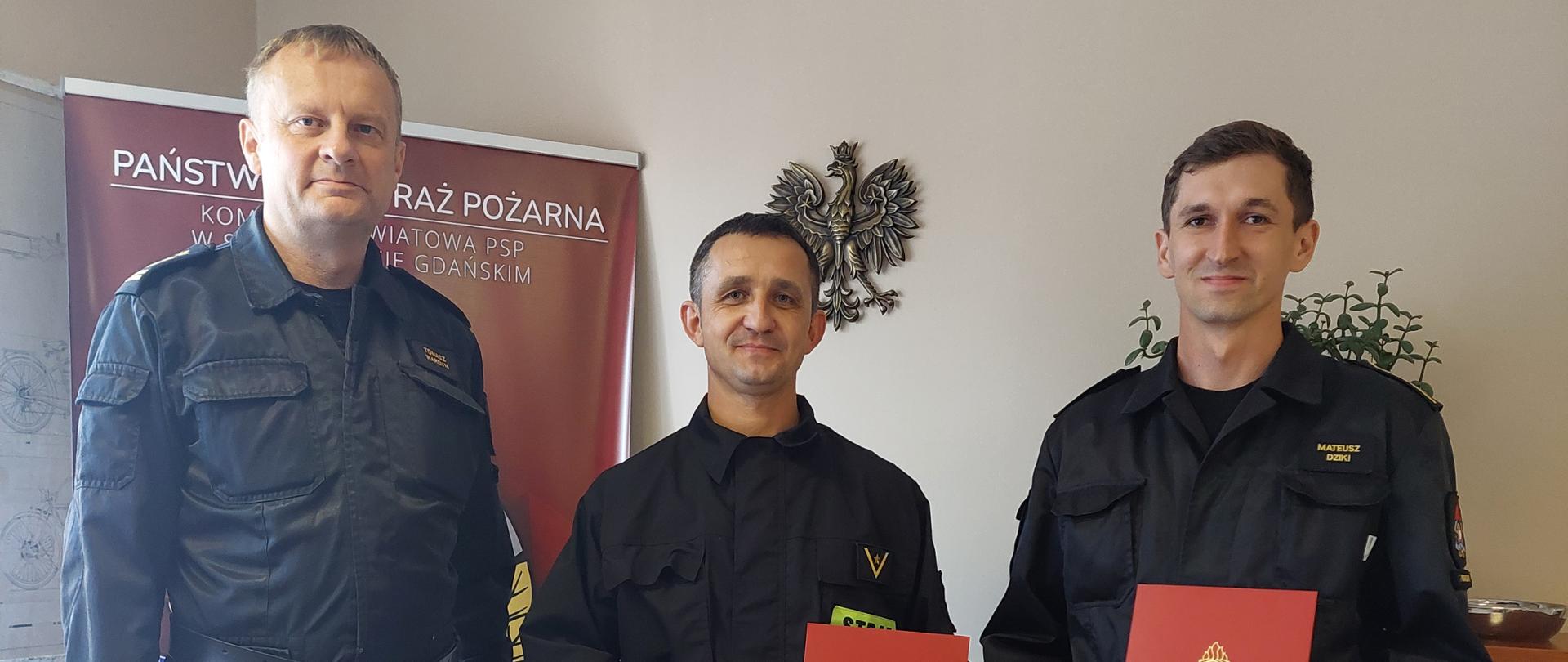 Zdjęcie przedstawia Komendanta Powiatowego PSP oraz nagrodzonych funkcjonariuszy, w tle baner PSP, godło