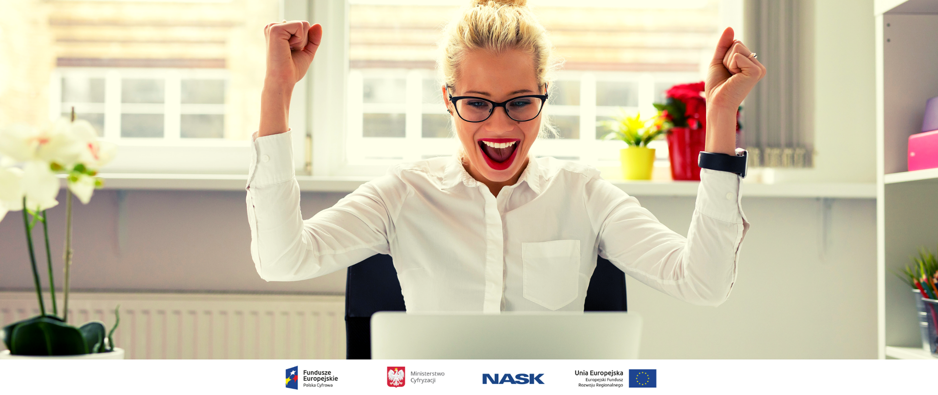 Dziewczyna siedząca przed komputerem. Unosi ręce w geście radości i zwycięstwa