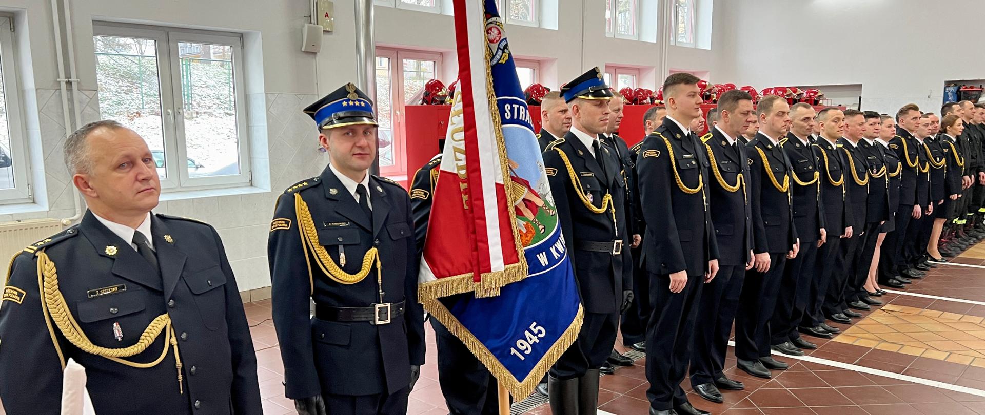 Pododdział stoi w garażu komendy w dwuszeregu podczas uroczystej zbiórki.