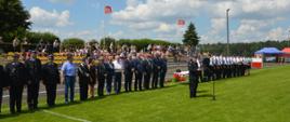 XI Powiatowe Zawody Sportowo-Pożarnicze OSP i MDP. Stadion w Miejskiej Górce. Na tle gości, komisji sędziowskiej i trybun, na których zasiadają kibice, do zebranych przemawia komendant powiatowy PSP w Rawiczu. Z prawej strony w oddali widoczne są namioty.