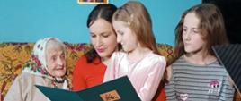 W pokoju na kanapie siedzą cztery osoby. Od lewej: Pani Anna Winiarska, jej prawnuczka (czyta list gratulacyjny od Prezesa KRUS) oraz dwie praprawnuczki.