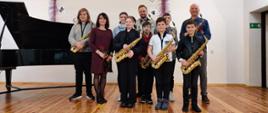 Zdjęcie grupowe podczas koncertu saksofonowego w dniu 19.04.2023 r. w auli szkoły. Na scenie klasa saksofonu oraz osoby dorosłe: od lewej strony - Halyna Hachak, Mateusz Boduch i Ryszard Żołędziewski.