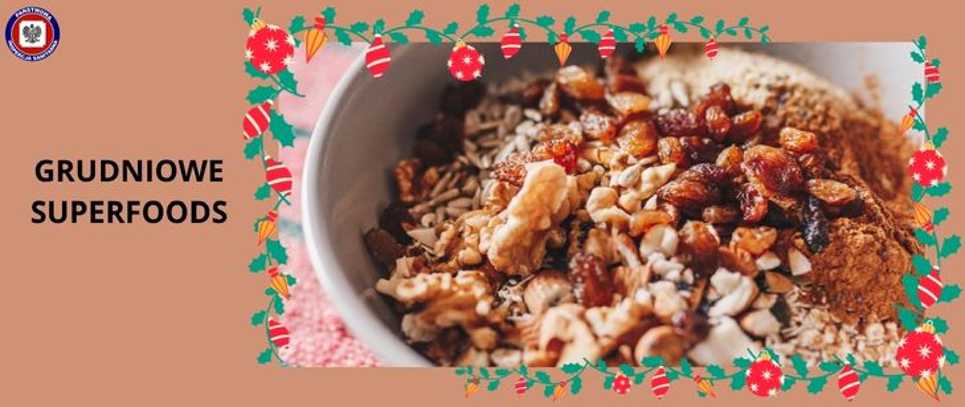Na brązowym tle w ramce przedstawiającej motyw świąt Bożego Narodzenia (zielone gałązki ostrokrzewu z widocznymi czerwonymi i pomarańczowymi ozdobami choinkowymi) w jasnym naczyniu mieszanka nasion i przypraw. Widoczne orzechy włoskie, słonecznik, suszona żurawina oraz rodzynki. W lewym górnym rogu logo Państwowej Inspekcji Sanitarnej. Po lewej na środku napis Grudniowe superfoods. 