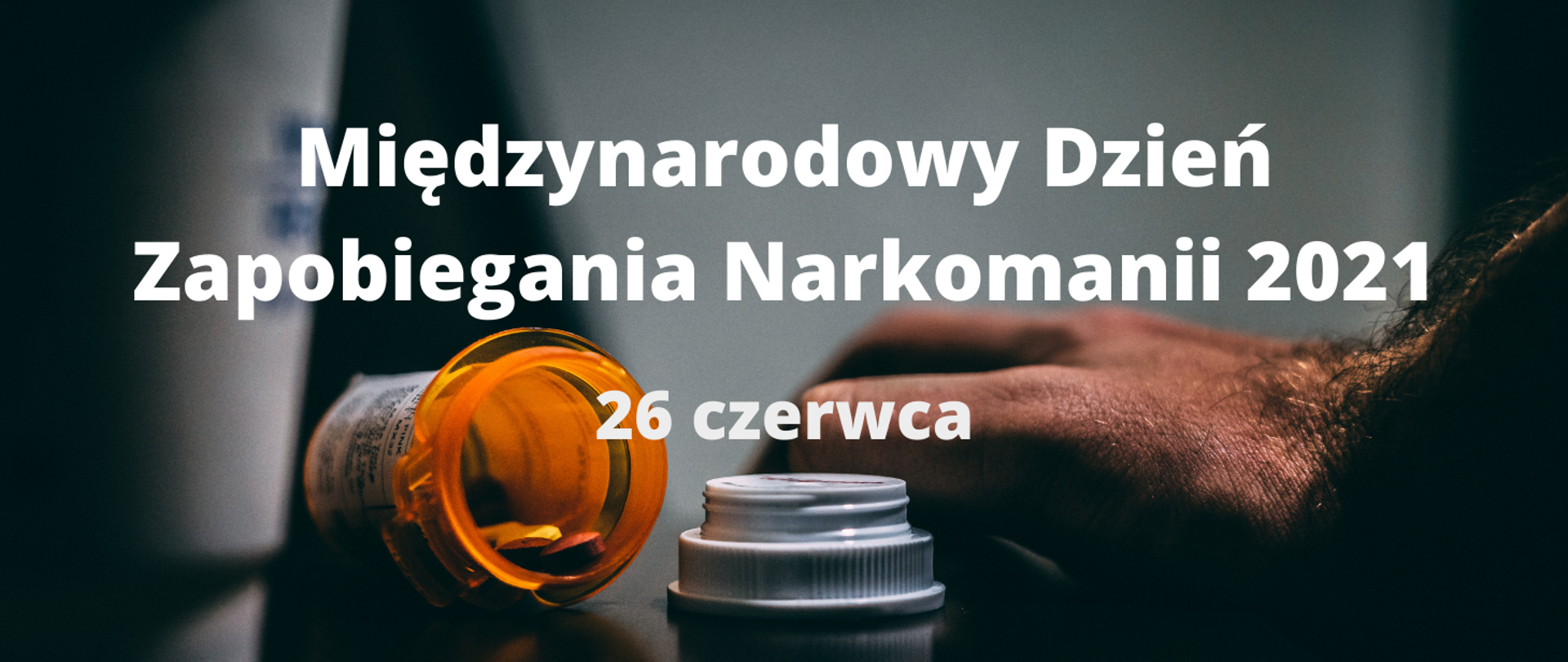 Grafika z tekstem: Międzynarodowy Dzień Zapobiegania Narkomanii 2021 26 czerwca. W tle otwarta fiolka z tabletkami i męska ręka.