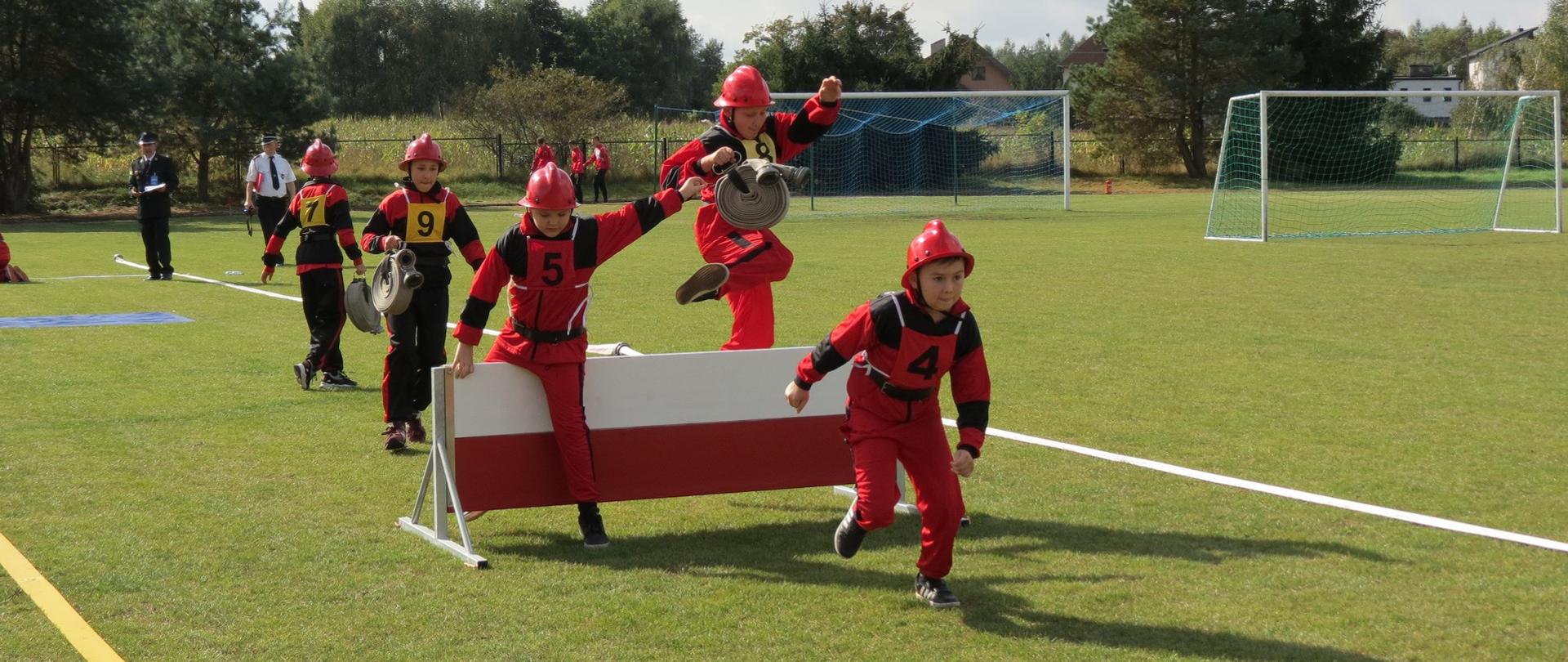 Zdjęcie przedstawia młodych zawodników drużyny MDP pokonujących płotek podczas konkurencji rozwinięcia bojowego.