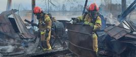 Strażacy PSP wynoszą spalone elementy z pogorzeliska.