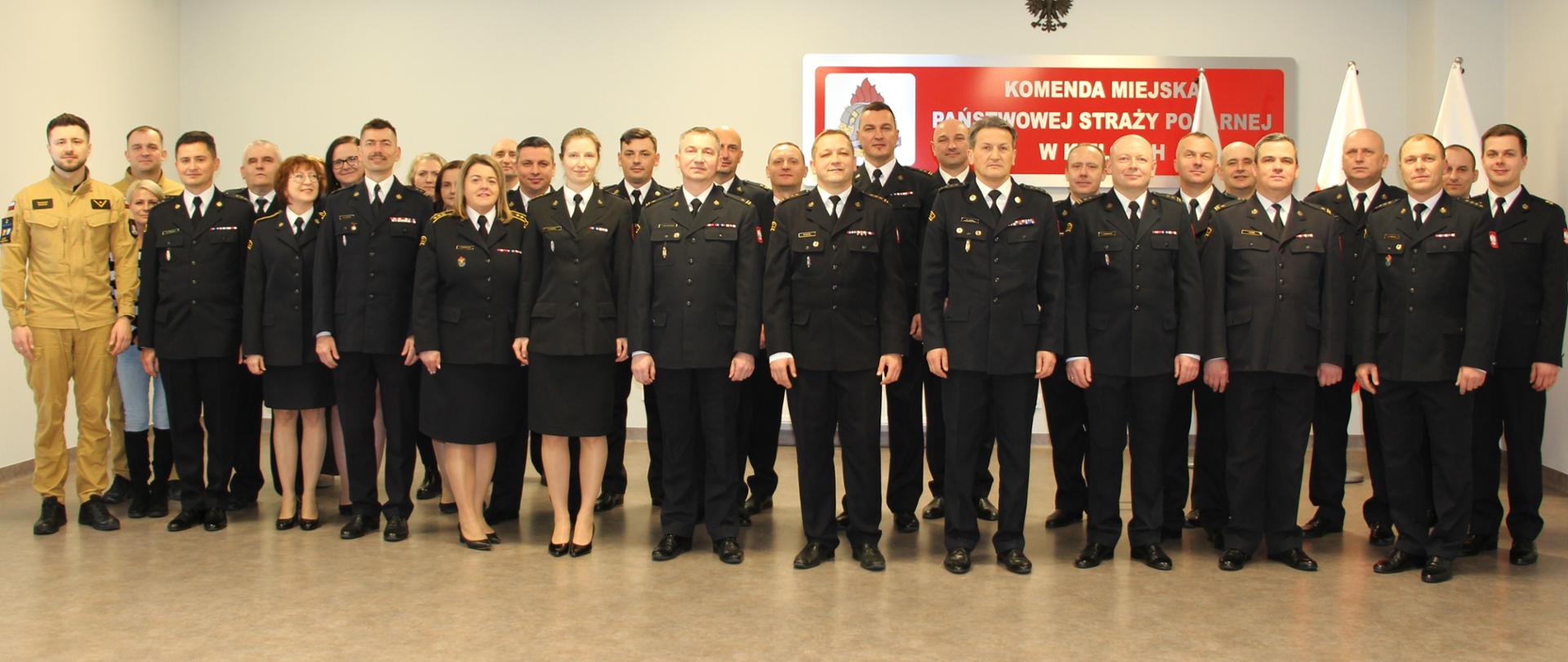 Fotografia przedstawia funkcjonariuszy i pracowników cywilnych ustawionych do pamiątkowego zdjęcia. W pierwszym rzędzie stoi kadra kierownicza tutejszej komendy oraz odchodzący i nowy zastępca komendanta miejskiego.