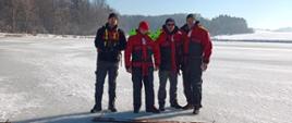 Na zdjęciu wycięta przerębel na jeziorze w kształcie trójkąta, obok boków trójkąta przykręcone do lodu deski zabezpieczające przed poślizgiem. Obok przerębli nurkowie instruktorzy wraz z zastępcą podkarpackiego komendanta wojewódzkiego PSP