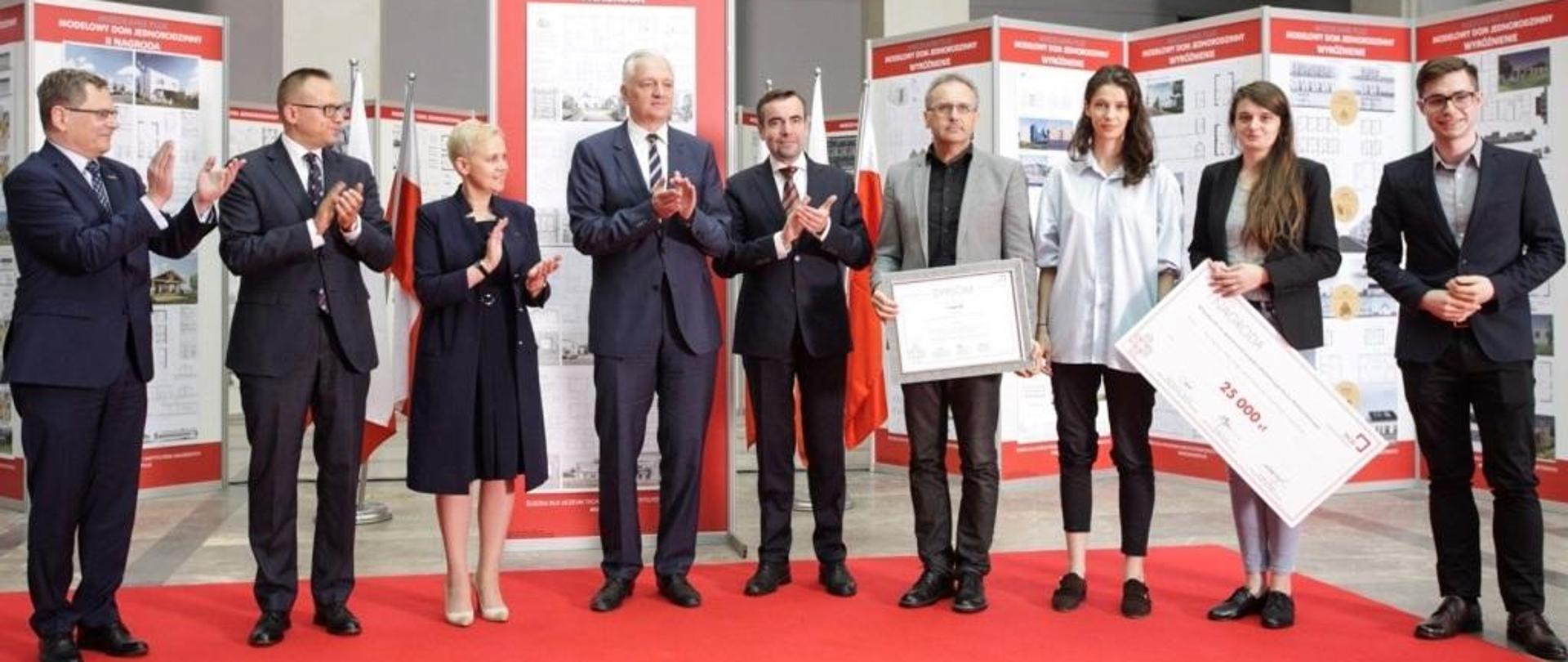 Minister Gowin w otoczeniu laureatów konkursu stoi na tle projektów prezentowanych na rozkładanych ściankach