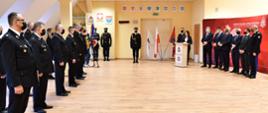 Zdjęcie przedstawia strażaków OSP dalej strażaków pocztu sztandarowego oraz kobietę przemawiającą przy mównicy obok osoby w garniturach oraz komendant wojewódzki