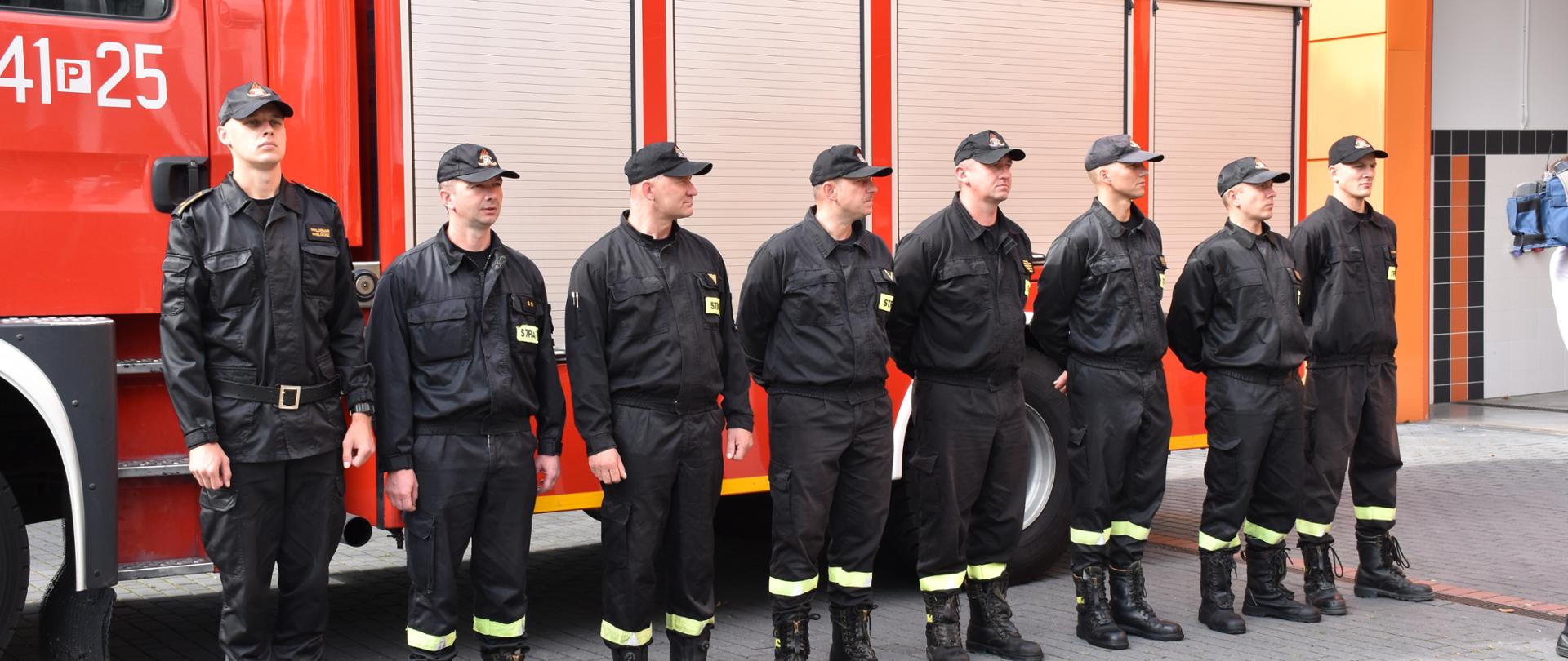 Strażacy stoją w szeregu przed samochodem