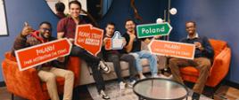 Pięciu młodych mężczyzn siedzi na kanapie i fotelach, pozując do zdjęcia z banerami reklamowymi programu stypendialnego