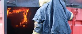 Strażak ubrany w ubranie specjalne i aparat ochrony dróg oddechowych szykuje się do wejścia do komory rozgorzeniowej - kontenera, w którym odwzorowano warunki pożarowe.