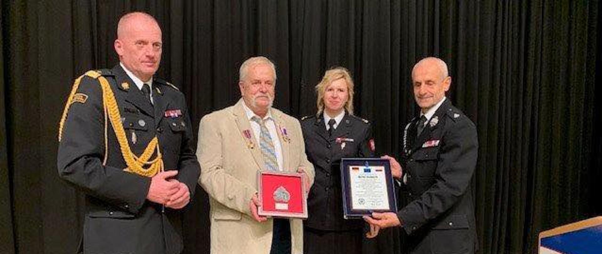 Zdjęcie grupowe, od lewej nadbryg. Jarosław Tomczyk, odznaczony Warner Hackbart, mł. bryg Agnieszk a Beśka-Mazurek oraz Dh. Marek Kowalski. W tle kurtyna.