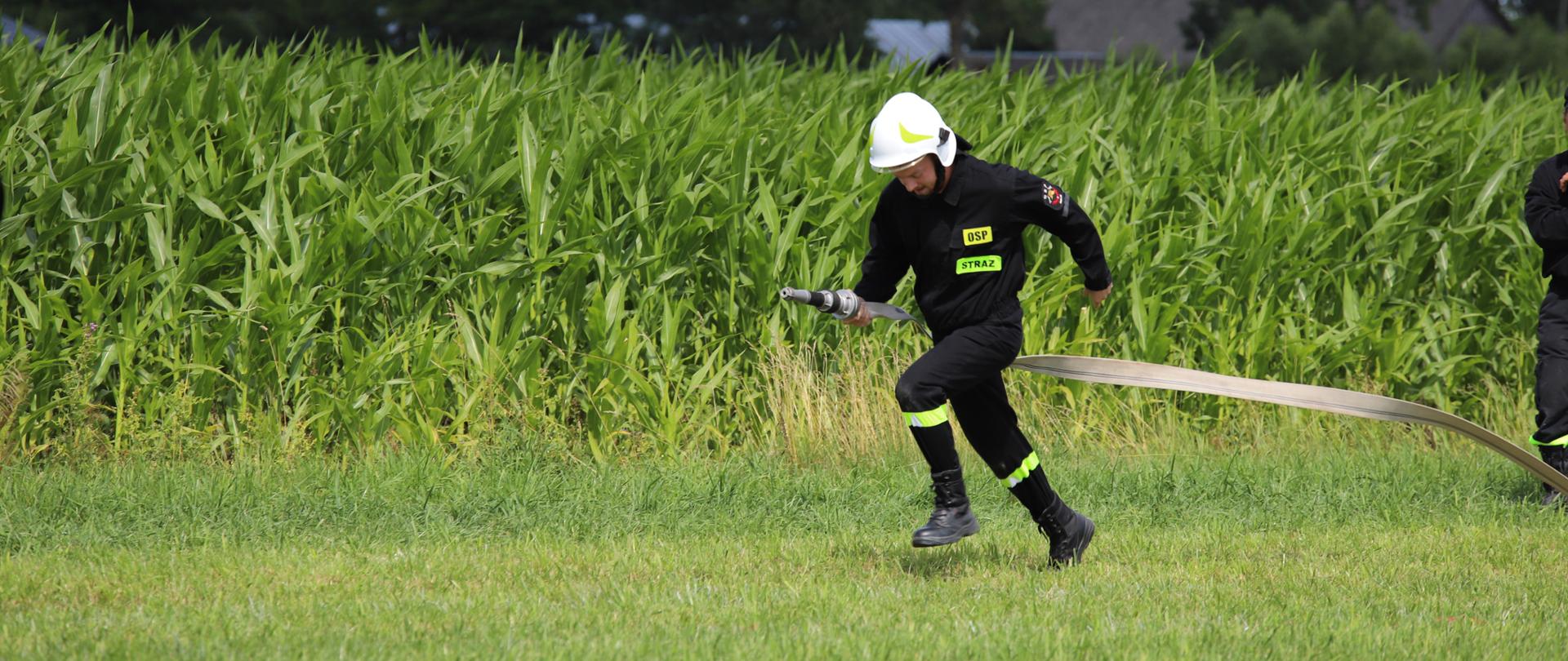 Zdjęcie przedstawia druha osp biegnącego z wężem i prądownicą 