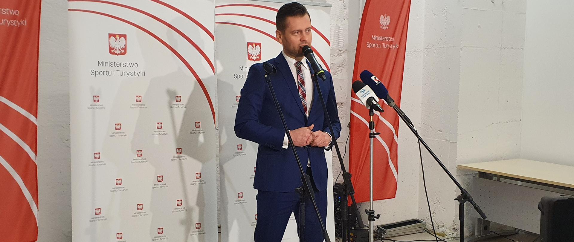 Minister Kamil Bortniczuk zapowiedział nowy program upowszechniania strzelectwa w Polsce. Na zdjęciu minister przemawia do mikrofonu, w tle ścianka z logotypami Ministerstwa Sportu i Turystyki.